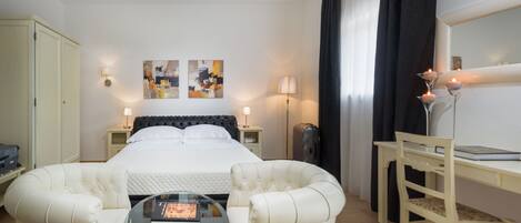 Habitación de hotel con cama, dos sillones, escritorio, lámpara y cuadros en la pared.