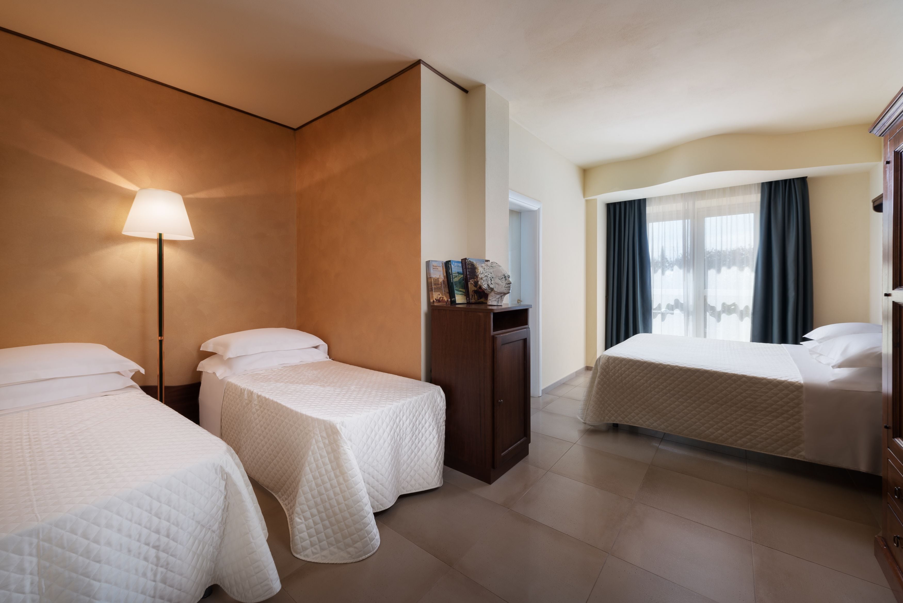Habitación de hotel con dos camas individuales, un escritorio con lámpara y vistas al exterior.