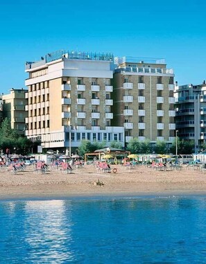 A multi-story hotel with balconies, a beach in the foreground, and beach umbrellas. - Hotel Napoleon (Gabicce Mare)