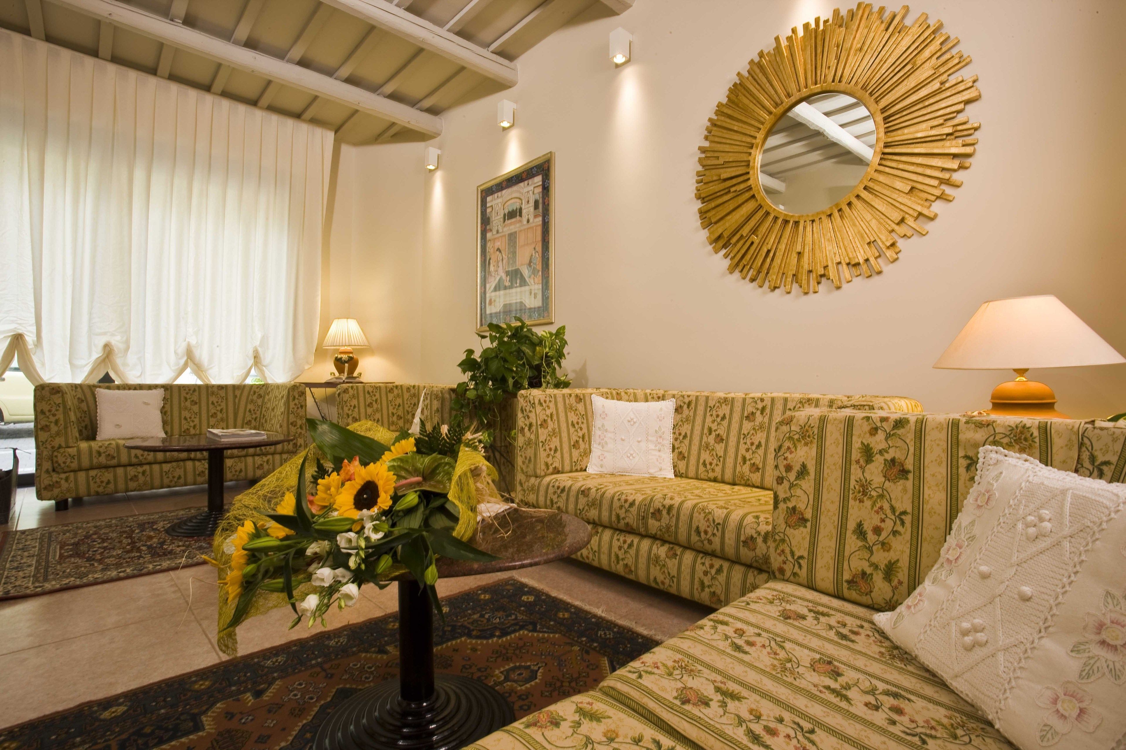 A living room with patterned sofas, a round mirror, and a floral arrangement.