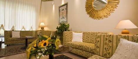 A living room with patterned sofas, a round mirror, and a floral arrangement.