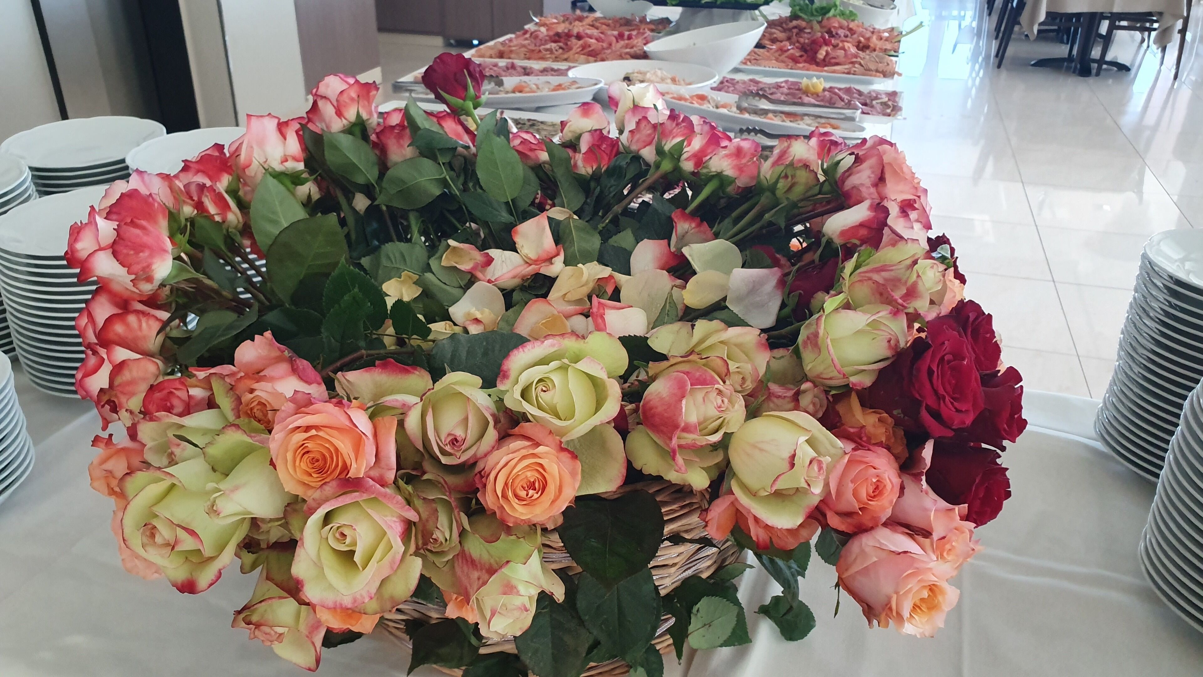 A table with a large floral arrangement of roses and a buffet with various dishes.