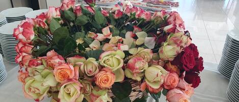 A table with a large floral arrangement of roses and a buffet with various dishes.