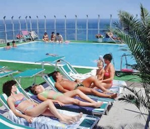 A pool area with lounge chairs and a view of the ocean. - Hotel Napoleon (Gabicce Mare)