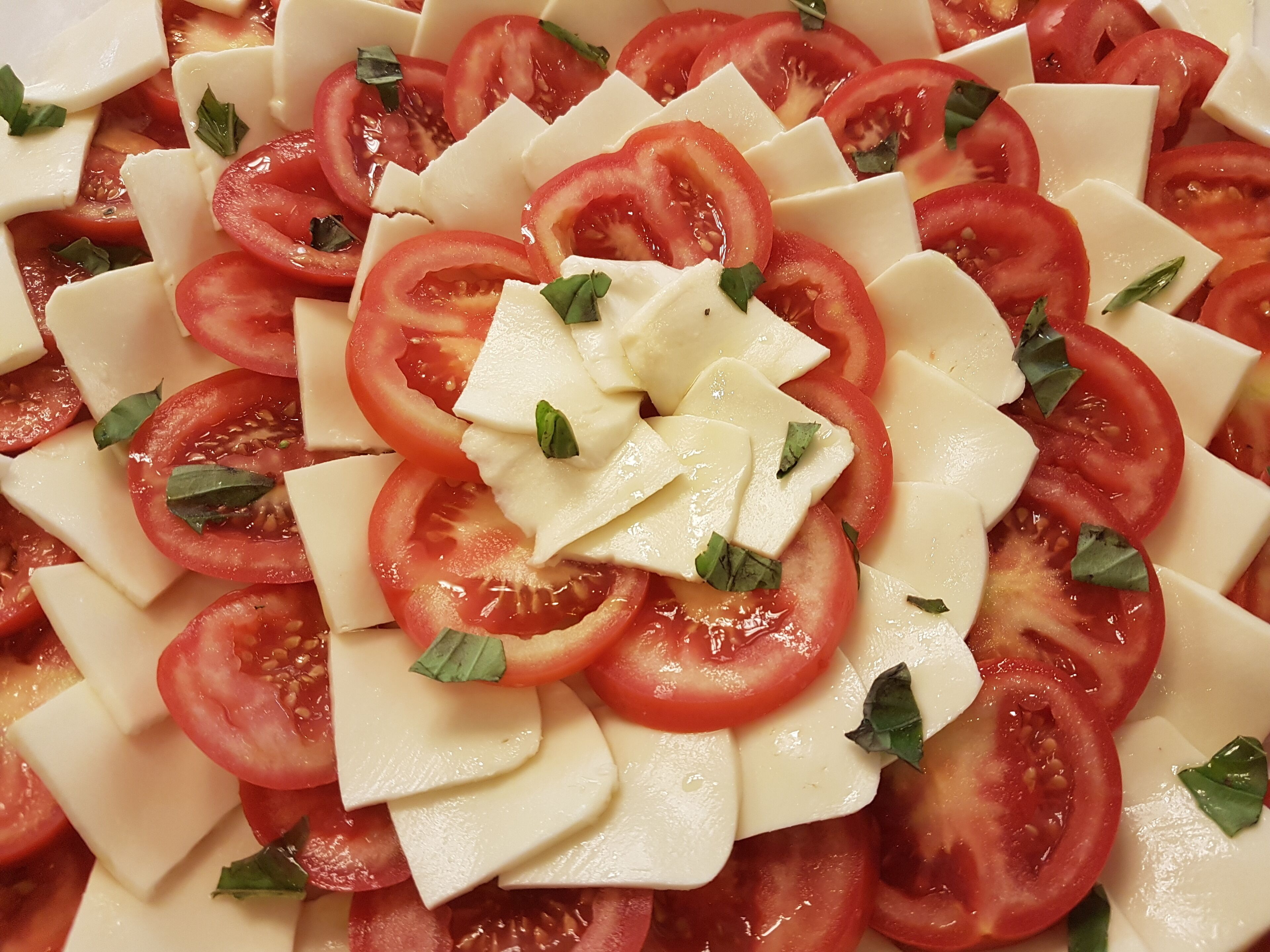 A close-up of a tomato and cheese salad with basil leaves.