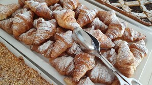 A tray of assorted pastries, including croissants and a dessert, with a spoon resting on them. - Hotel Napoleon (Gabicce Mare)