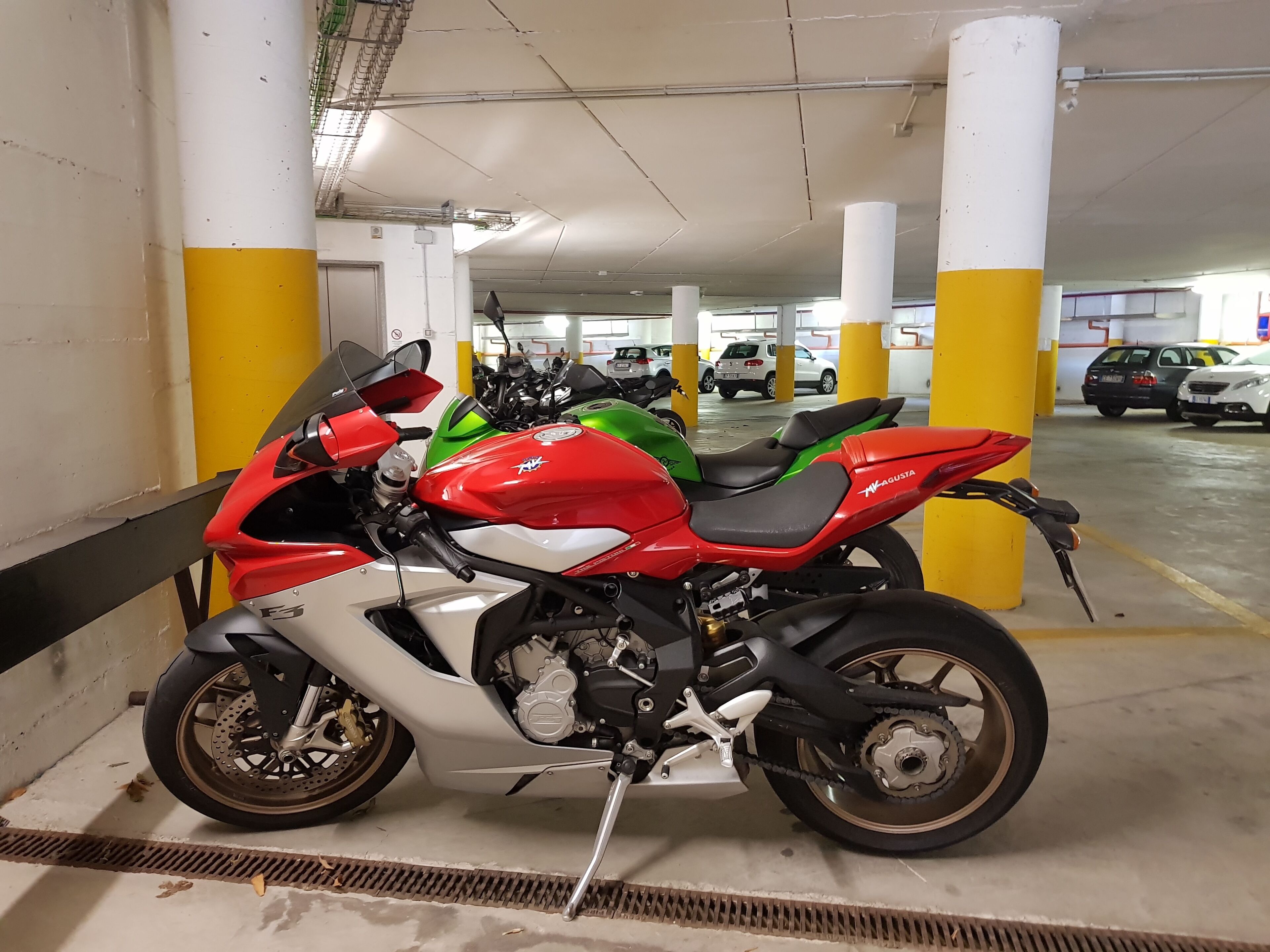 Una motocicleta estacionada en un estacionamiento de varios niveles con pilares amarillos y pisos de concreto.