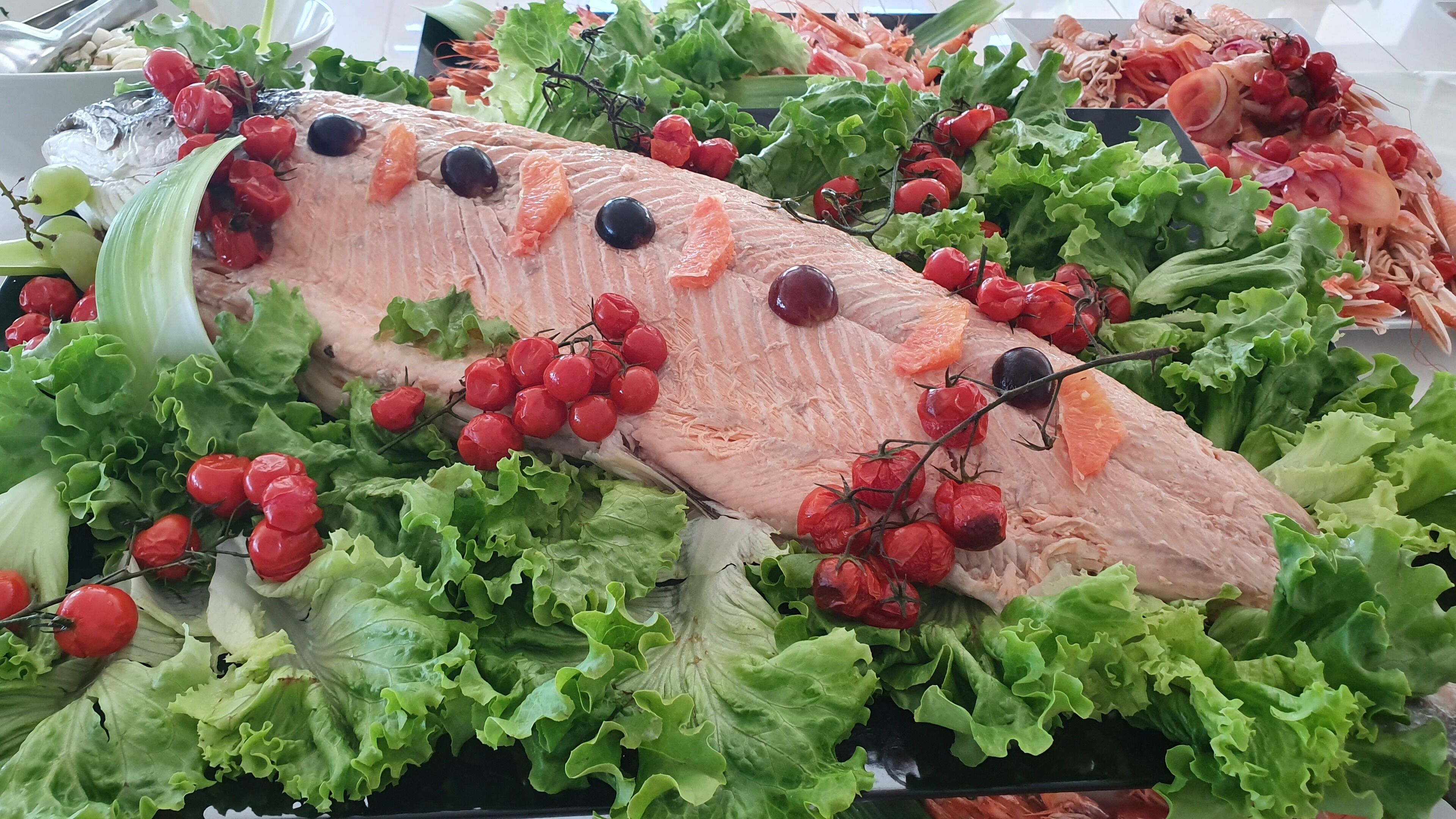 A large fish centerpiece surrounded by fresh vegetables and herbs.