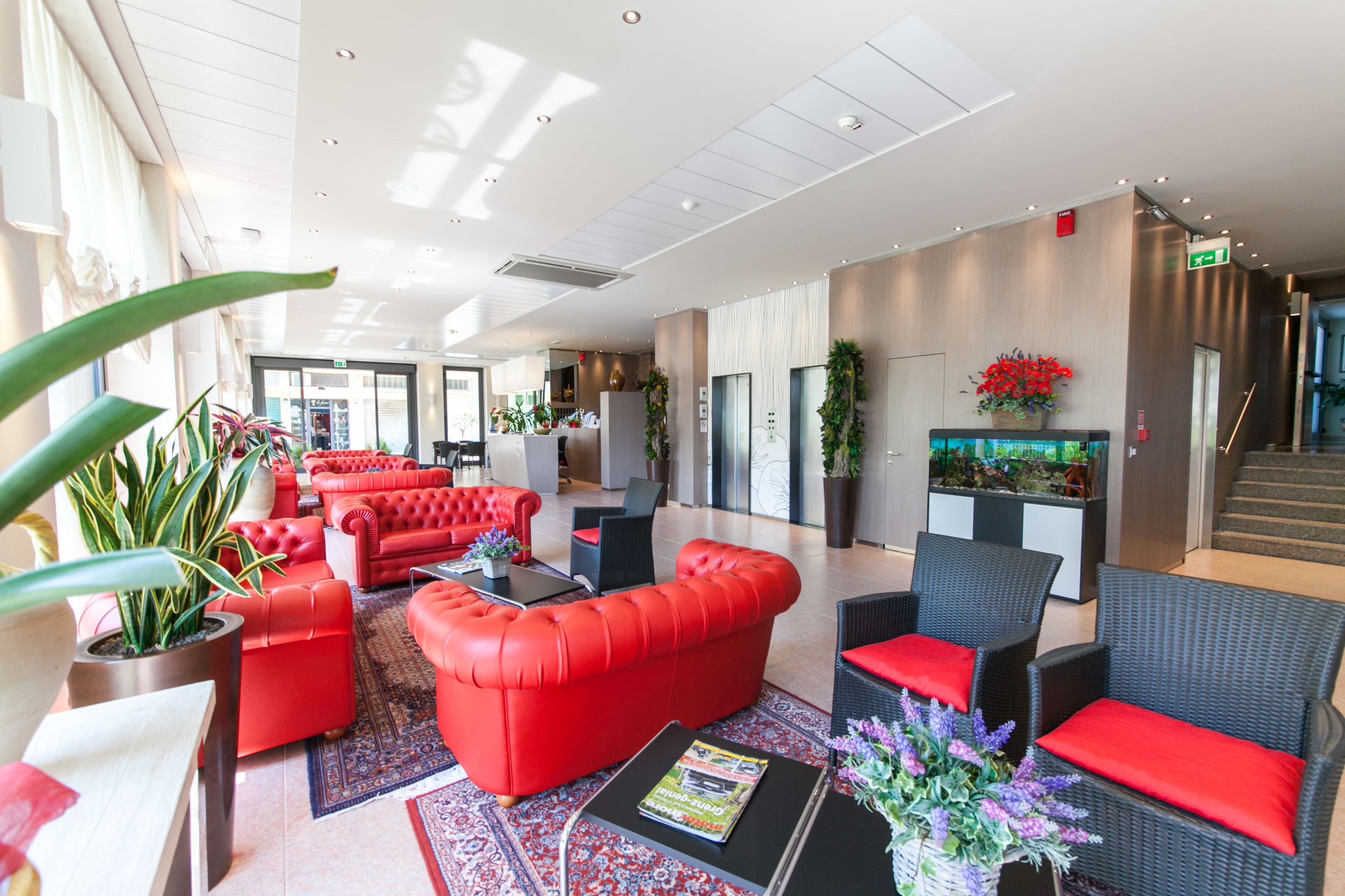A spacious lobby with red sofas, black chairs, and a reception desk.