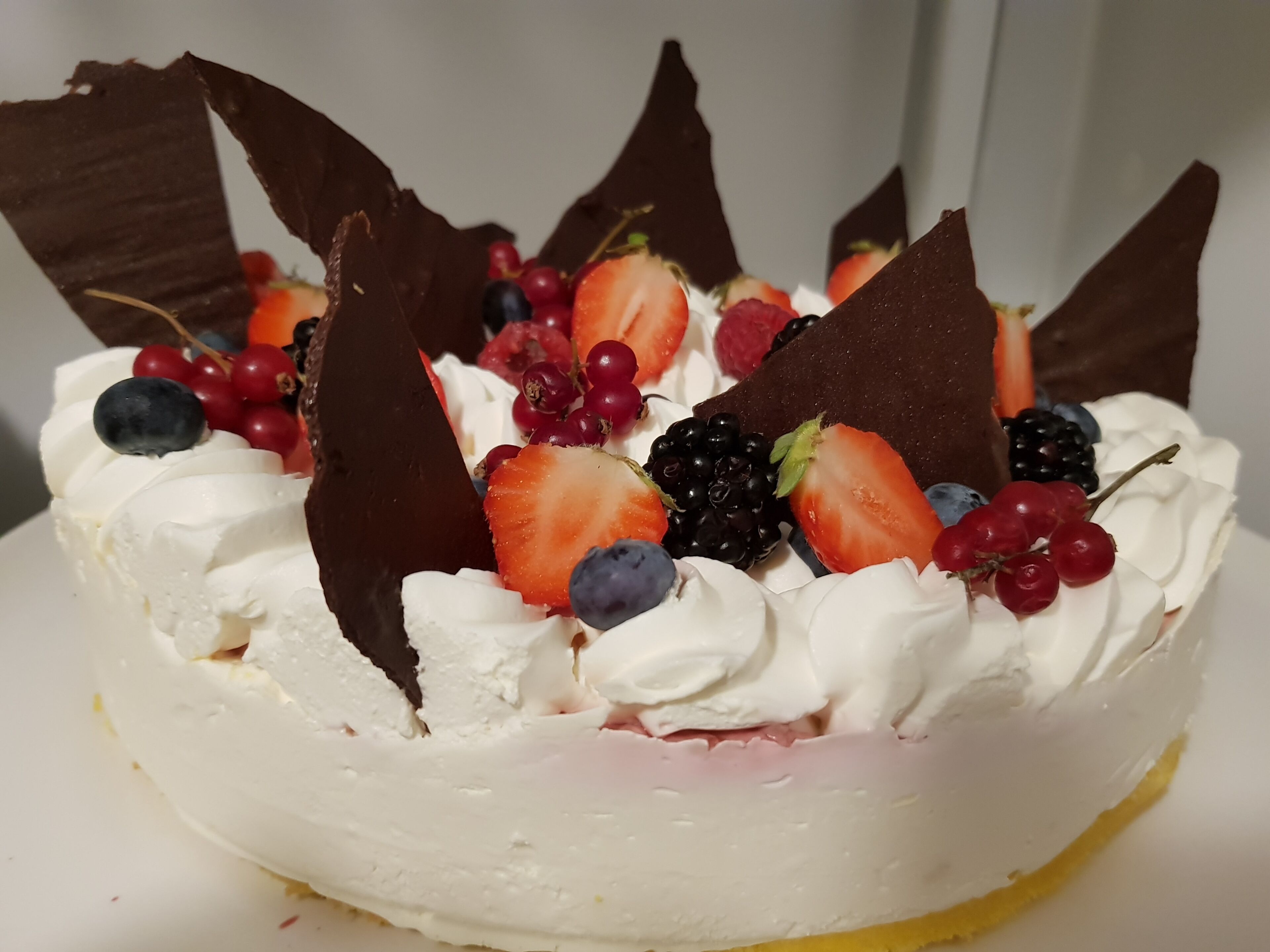 A dessert with whipped cream, strawberries, blueberries, blackberries, and chocolate pieces.