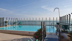 A pool area with clear blue water, a glass barrier, and lounge chairs. - Hotel Napoleon (Gabicce Mare)