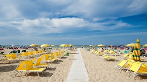 A beach with rows of yellow sun loungers and umbrellas, a clear sky, and a sandy path leading to the water. - Hotel Napoleon (Gabicce Mare)