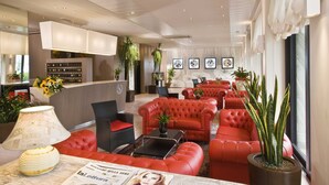A hotel lobby with red leather sofas, a reception desk, and various plants. - Hotel Napoleon (Gabicce Mare)