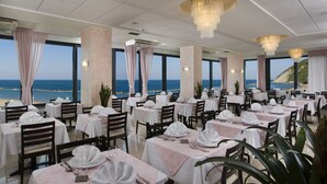 A restaurant with tables set for dining, large windows offering a view of the sea, and elegant chandeliers. - Hotel Napoleon (Gabicce Mare)