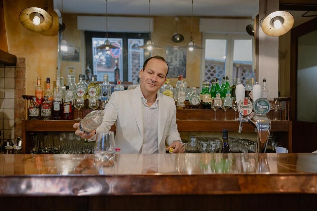 Zona de bar con un cantinero, estantes con varias botellas de licor y una barra.