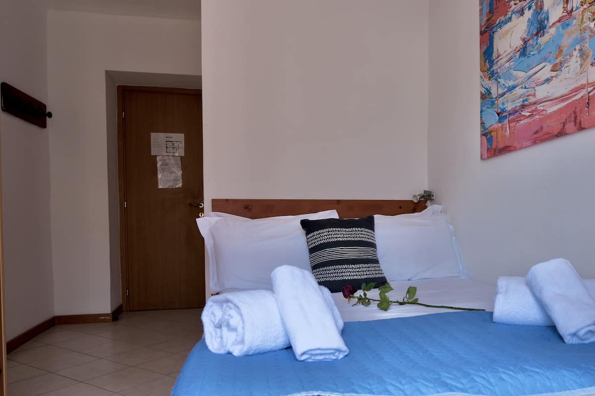 A hotel room with a bed, white towels, a blue bedspread, a black and white pillow, and a painting on the wall.
