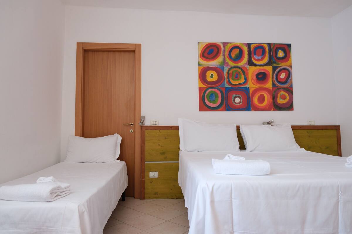 A hotel room with two beds, a wooden door, and a colorful abstract painting on the wall.