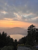 A panoramic view of a lake surrounded by hills and trees, with a clear sky and the sun setting or rising.