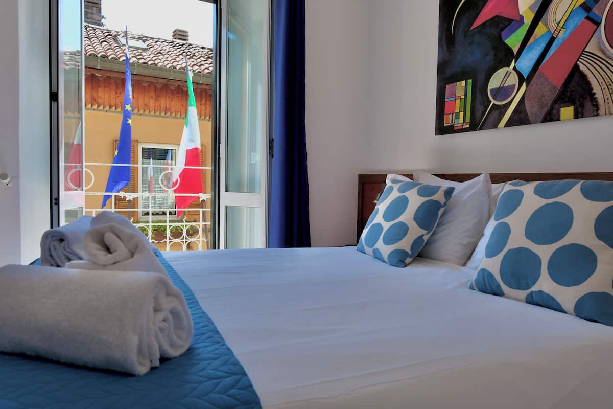 A hotel room with a bed, a painting, and a view of flags outside.