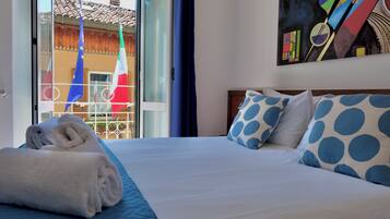 A hotel room with a bed, a painting, and a view of flags outside.