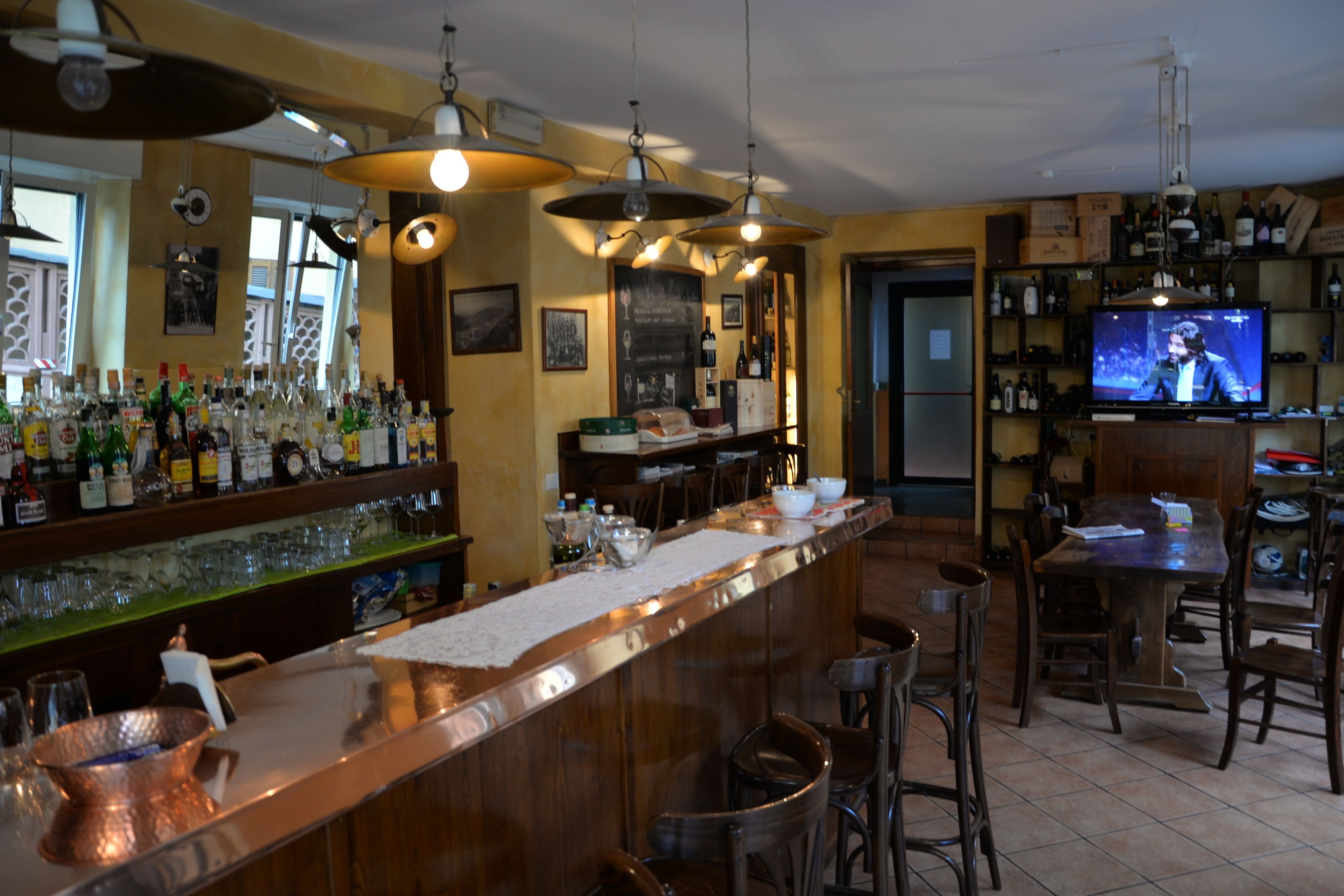 Un espace bar doté d’un long comptoir, de plusieurs luminaires suspendus et d’un écran de télévision diffusant une émission.