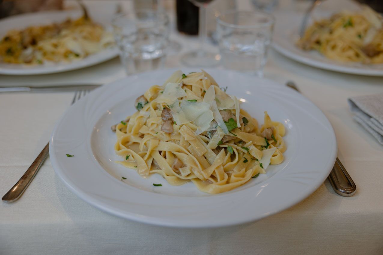 A plate of pasta with a creamy sauce, garnished with herbs, on a white tablecloth.