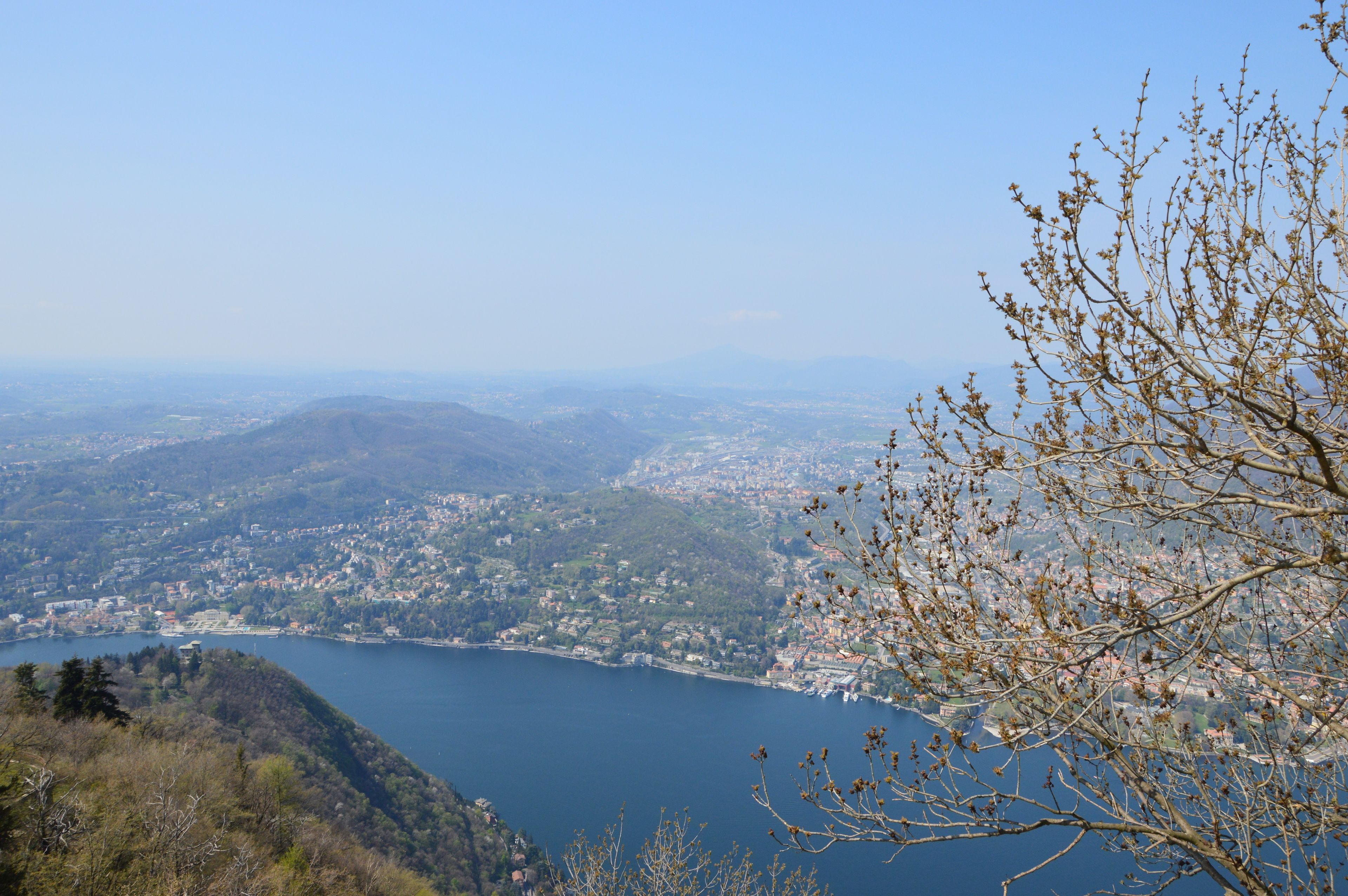 A panoramic view of a coastal town with a large body of water, surrounded by hills and mountains.