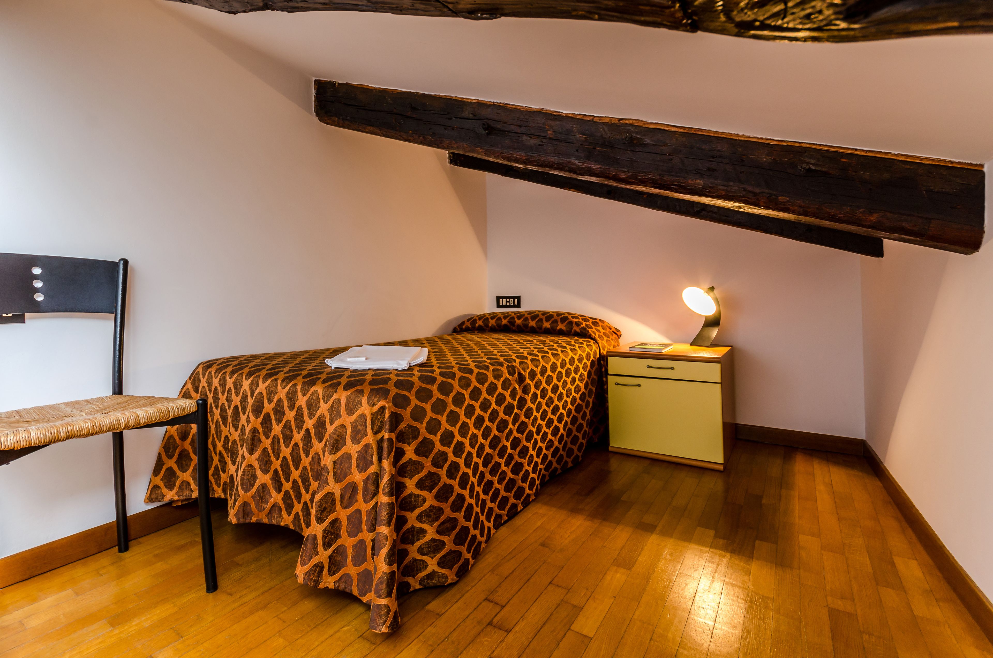 A small, cozy bedroom with a bed, bedside table, and a chair.