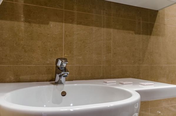 Un baño con un lavamanos blanco, un grifo moderno y una pared con azulejos color beige.