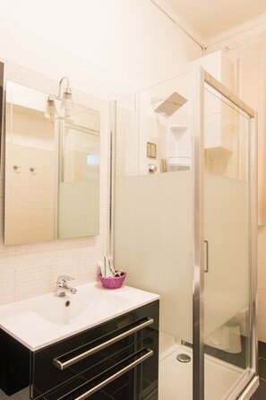 A bathroom with a white sink, a mirror, a glass shower enclosure, and a black vanity. - Hotel Alpi Resort (Turin)