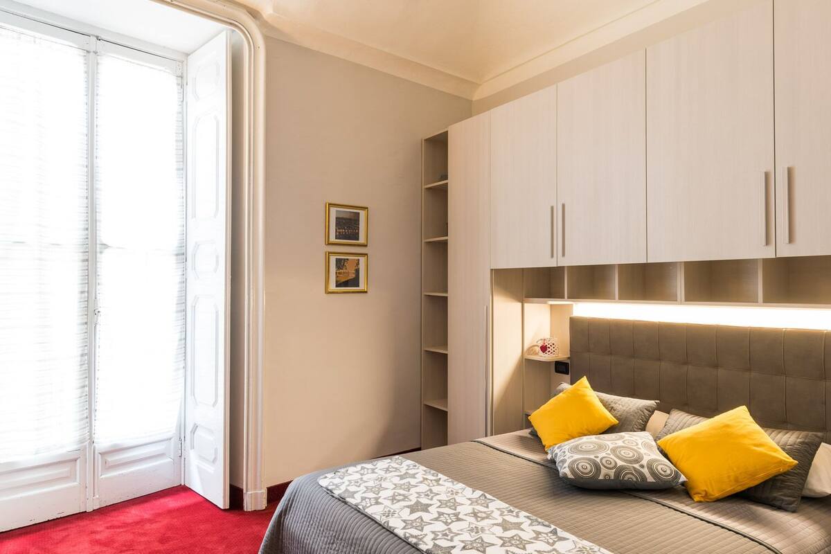 A bedroom with a bed, a red carpet, a sliding glass door, and a wardrobe with built-in lighting.