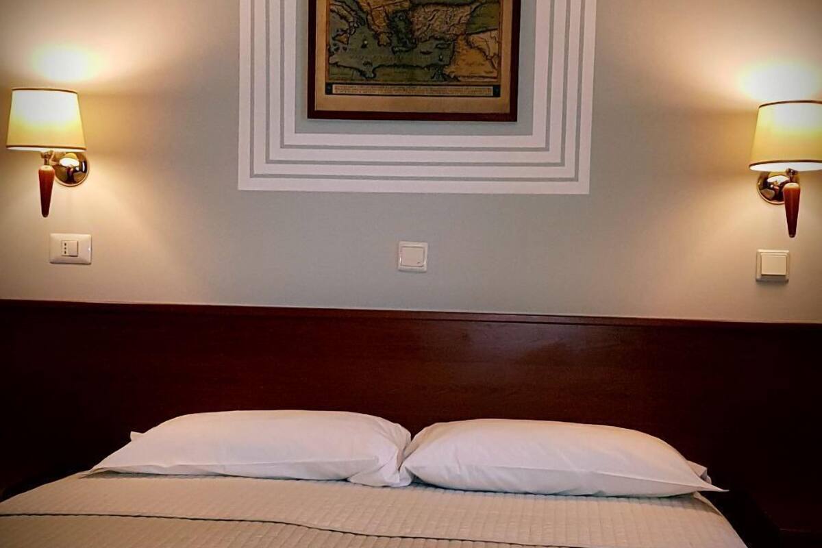 A hotel room with a large bed, two wall-mounted lamps, and a framed map on the wall.