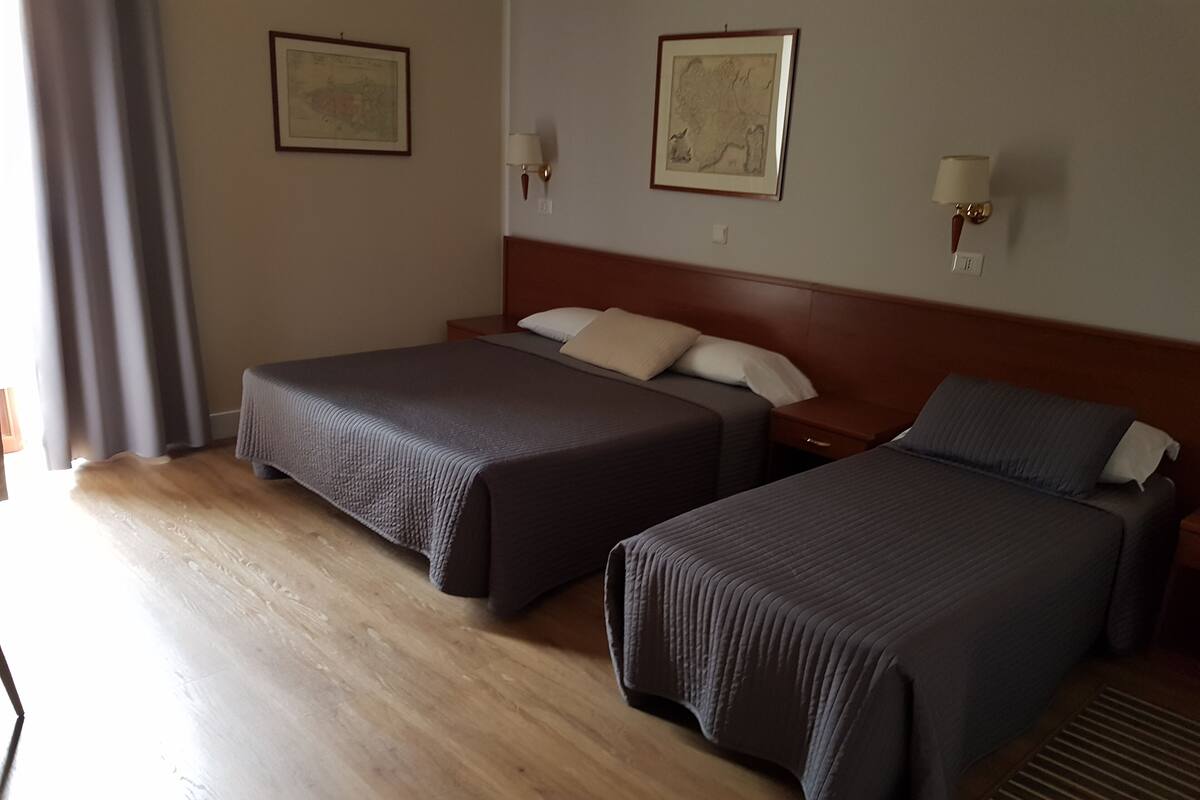 A hotel room with two beds, wooden flooring, and two wall-mounted lamps.