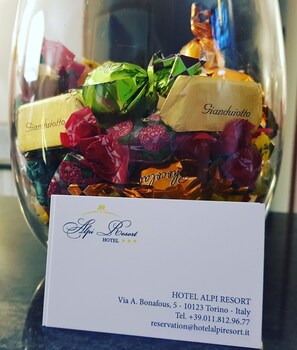 A glass vase filled with colorful candies and a business card for Hotel Alpi Resort. - Hotel Alpi Resort (Turin)