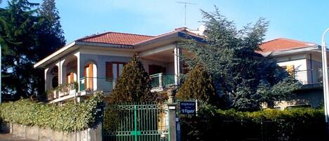 A two-story house with a red-tiled roof, a balcony, and a gated entrance.