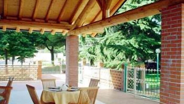 En udendørs terrasse med et træpergola, murstensvægge og et bord med stole.