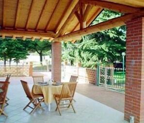 Un patio esterno con una pergola in legno, pareti in mattoni e un tavolo con sedie.
