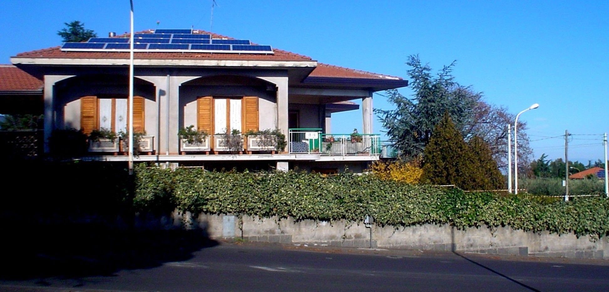 A building with a flat roof, solar panels, and a balcony with potted plants.