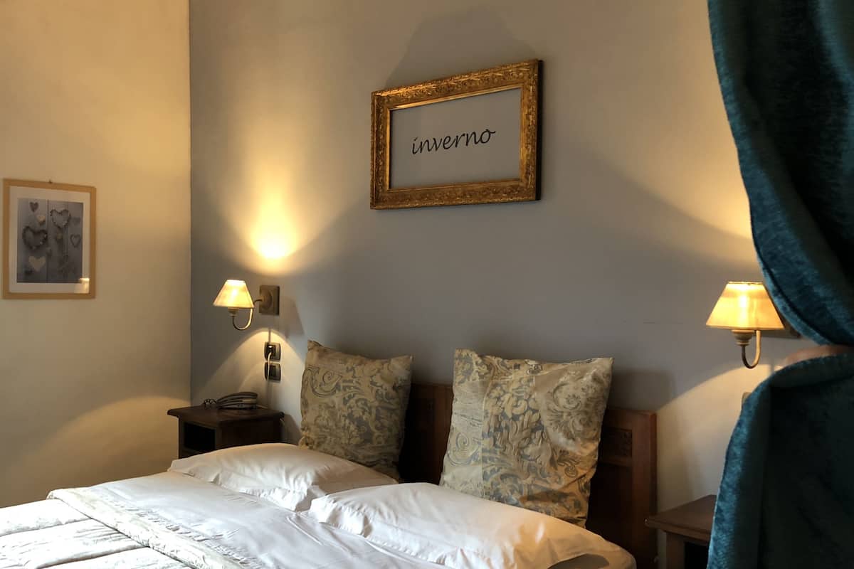 A hotel room with a bed, two wall-mounted lamps, a framed picture, and a decorative pillow.