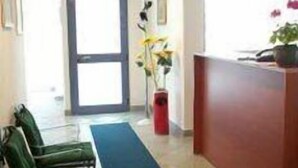 A reception area with a reception desk, a blue carpet, green chairs, and a potted plant. - Girasole House (Florence)