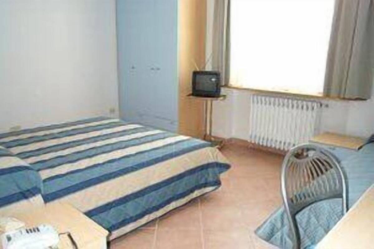 A small, sparsely furnished room with a bed, a chair, a small table, and a television.
