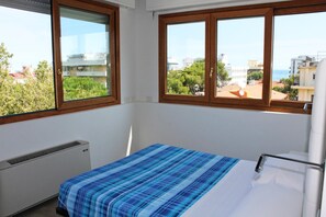 A bedroom with a bed, a radiator, and two windows with views of buildings and trees. - Hotel Saint Tropez Riccione (Riccione)