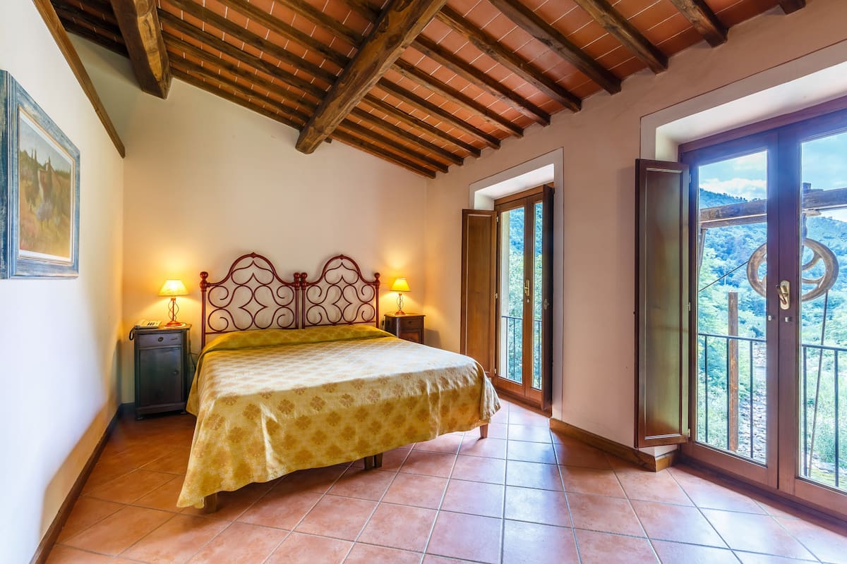 A bedroom with a bed, two bedside tables with lamps, a wooden ceiling, and a balcony with a view.