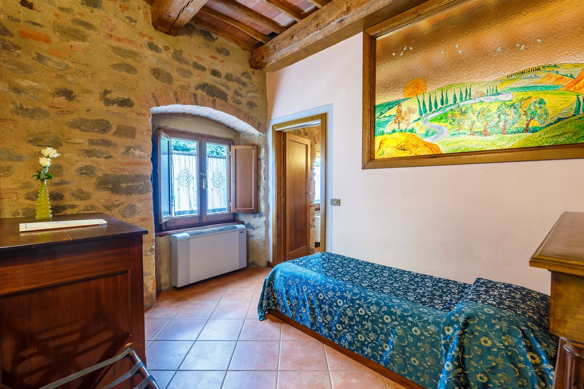A room with a bed, a desk, a radiator, and a painting on the wall.