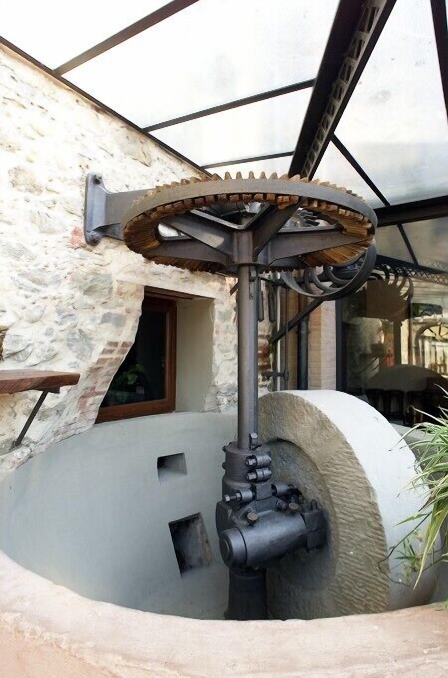 A mechanical gear system with a stone wall and a window in the background.