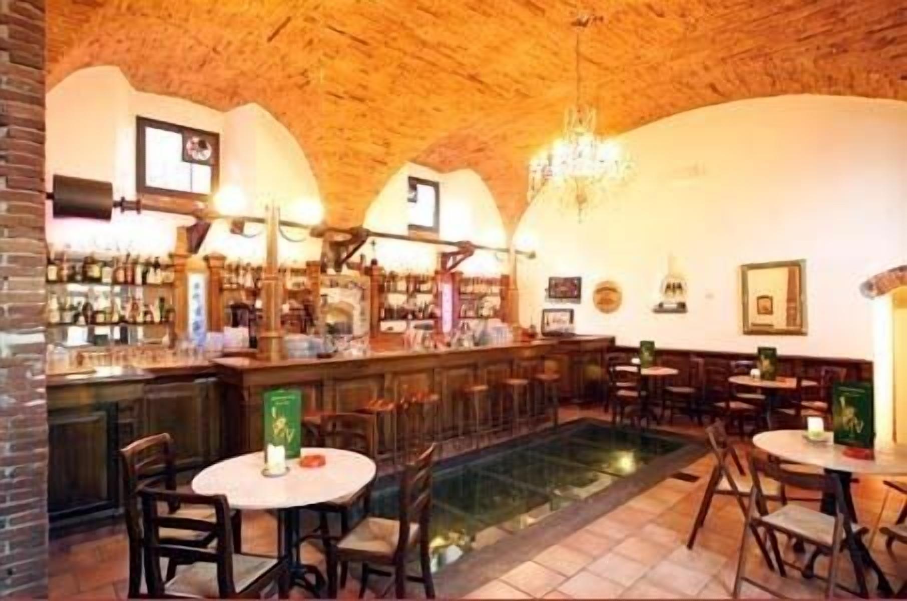 Ein Barbereich mit Holzbalkendecke, Ziegelwänden und einer zentralen Bar. Mehrere Tische und Stühle bieten Sitzgelegenheiten.