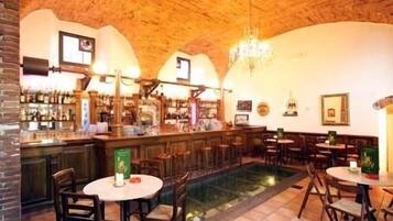 Ein Barbereich mit Holzbalkendecke, Ziegelwänden und einer zentralen Bar. Mehrere Tische und Stühle bieten Sitzgelegenheiten.