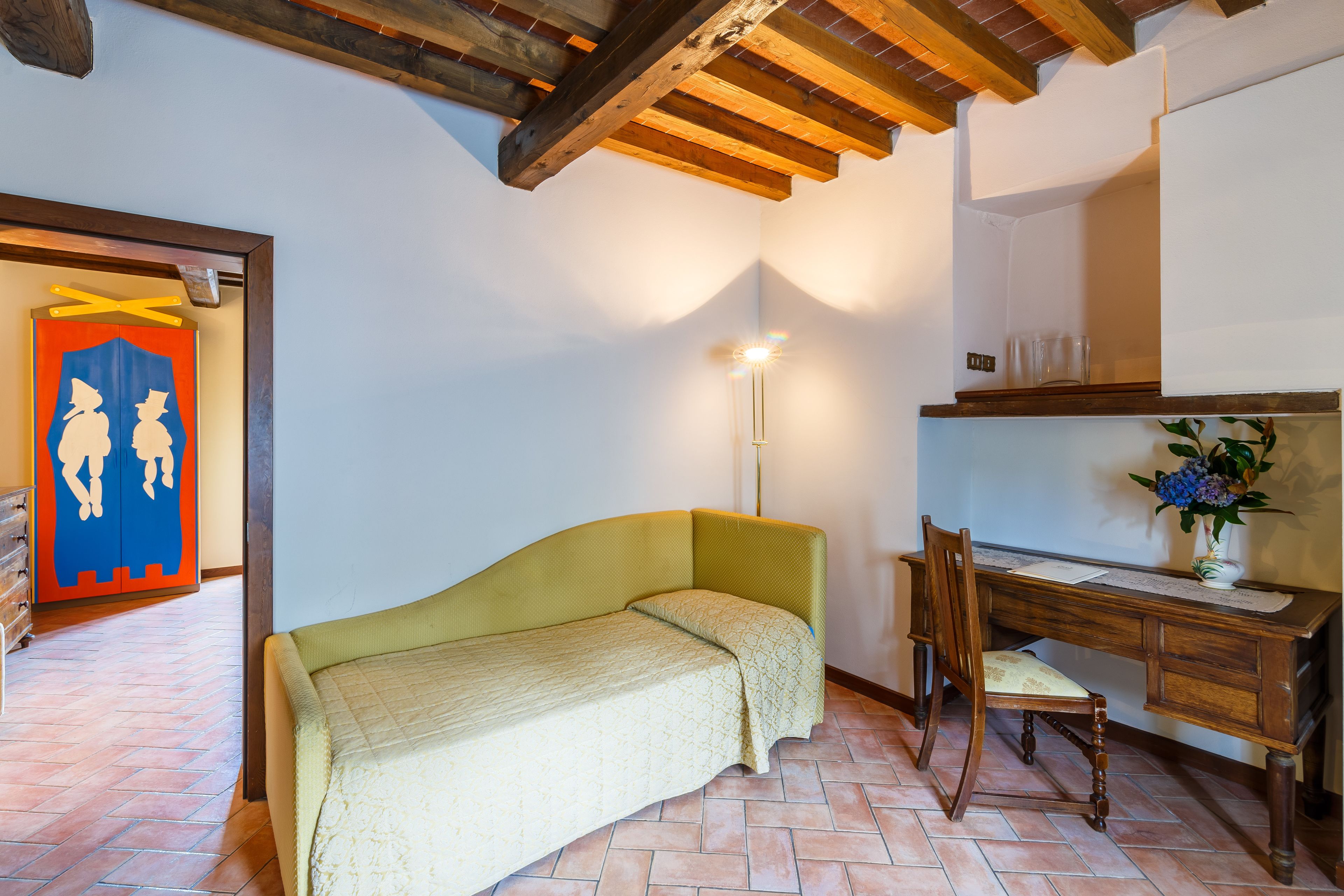Une pièce comprenant un lit, un bureau et une chaise. Le plafond est en bois et le sol est carrelé.