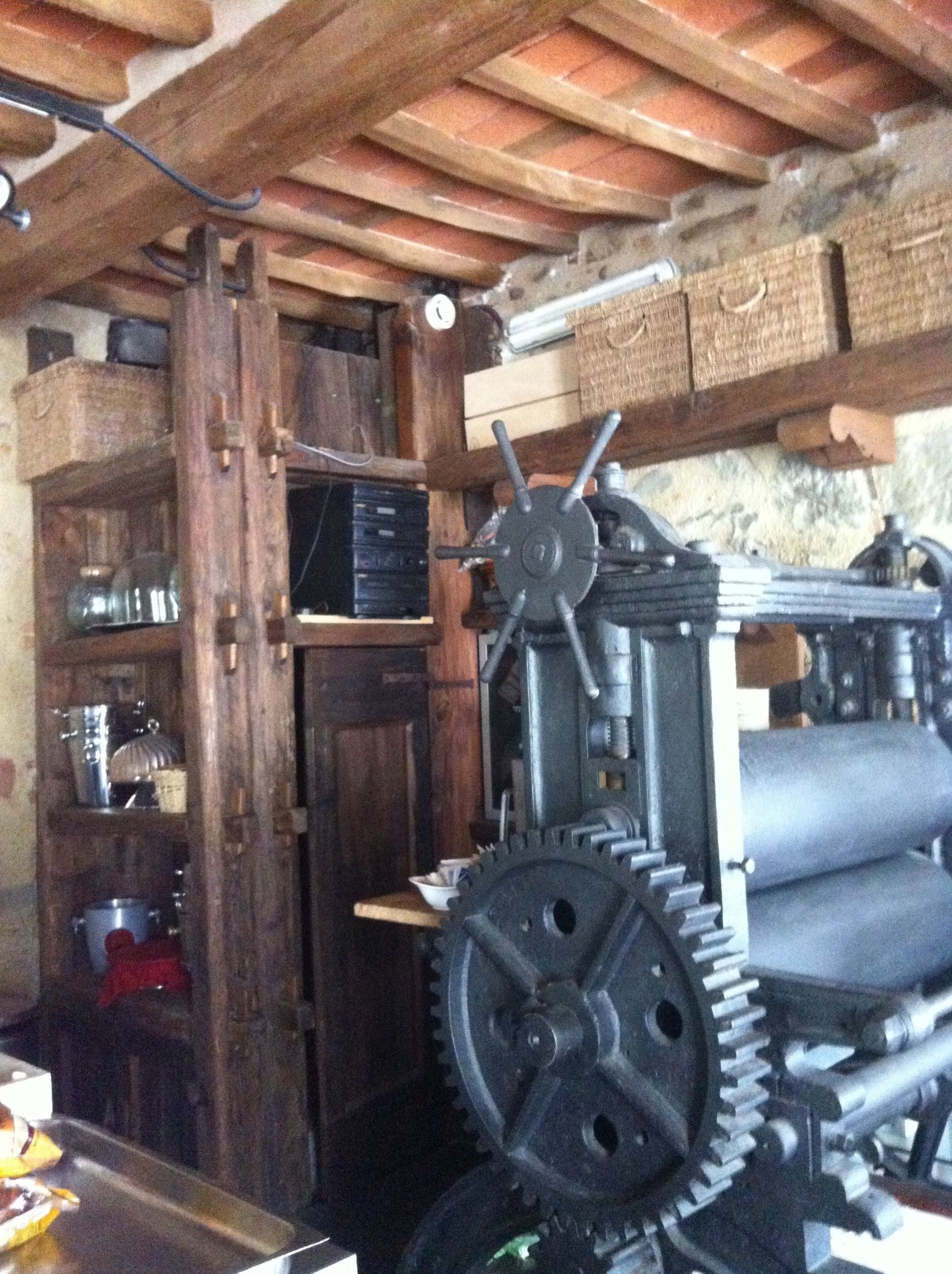 A rustic kitchen with wooden beams, a large mechanical device, and shelves with kitchenware.