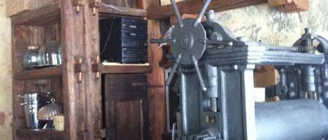 A rustic kitchen with wooden beams, a large mechanical device, and shelves with kitchenware.